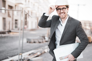 Freudig lächelnder Architekt auf der Baustelle mit Bauplänen 