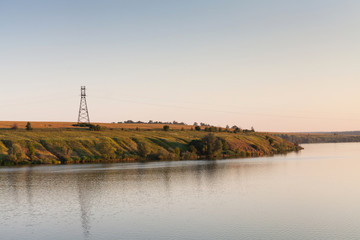 Fototapeta premium Summer evening landscape of the river and coastline with power lines high voltage tower with sunset sky background.