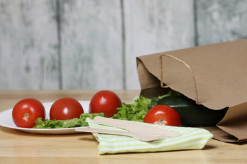 ingredients for cooking. Fresh vegetables on a wooden table. Tomato and salad. Ecology products. Recycle paper bag. Wooden recycle fork and knife