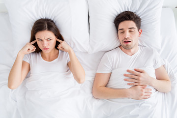 High angle above view photo of pretty lady covering ears handsome snoring guy couple lying sheets...