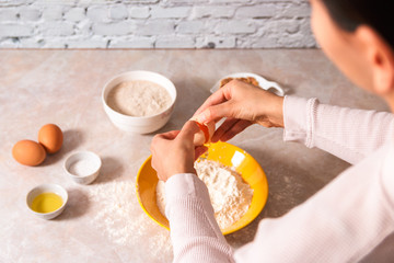 homemade bread baking. closeup woman hands adding egg in flour, dough preparation in bright kitchen with marble countertop