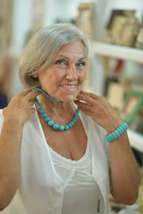 Beautiful smiling senior woman at souvenir store trying on necklace