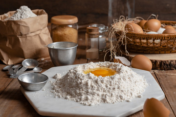 Flour with yolk egg and A lot of eggs put in the basket are placed on the wooden table for cooking something.