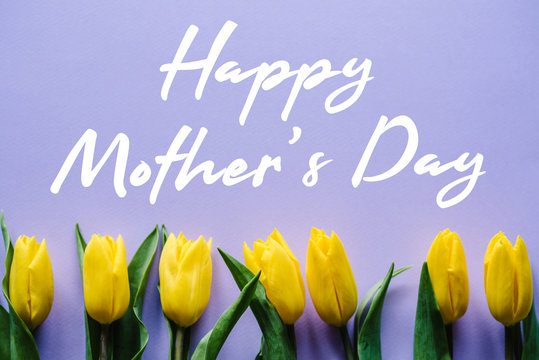 Happy mother's day. Text sign with yellow tulips on violet background.  Floral greeting card concept. Sensual tender women image. Holiday greeting card for Mother's Day! Top view, flat lay.