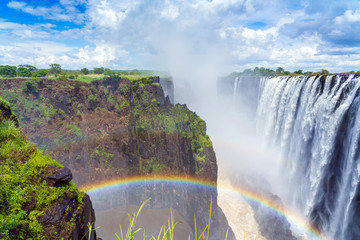 Panorama view with dramatic clouds and waterfall  with a rainbow at Victoria Falls on the Zambezi River, Zimbabwe, Zambia. - Powered by Adobe