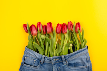 A bouquet of red tulips peeks out of pants or shorts on a yellow background. The concept of a healthy diet, a beautiful body, youth, weight loss or losing weight.