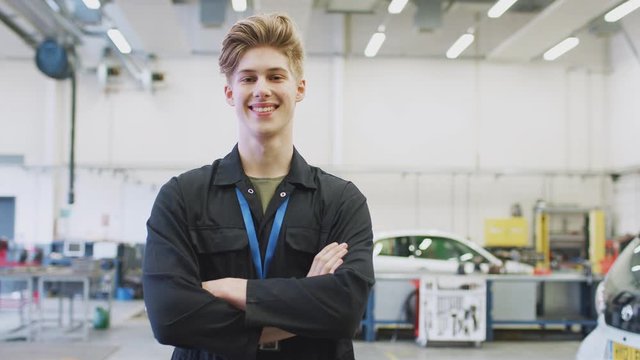 Portrait of male student studying for auto mechanic apprenticeship at college folding arms and smiling at camera - shot in slow motion