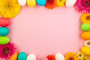 Beautiful easter eggs painted in yellow, red and green pastel colors on a pink background in a composition with fresh flowers.