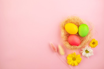 Fototapeta na wymiar Beautiful easter eggs painted in yellow, red and green pastel colors on a pink background in a composition with fresh flowers.