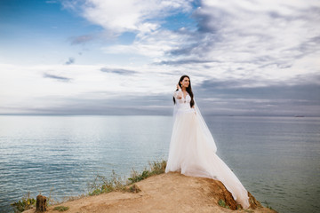 Fototapeta na wymiar Romantic beautiful bride in white dress posing on terrace with sea and mountains in background