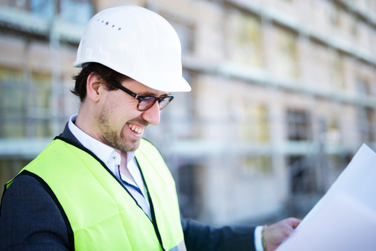 Freudig l&auml;chelnder Architekt auf der Baustelle mit Baupl&auml;nen 