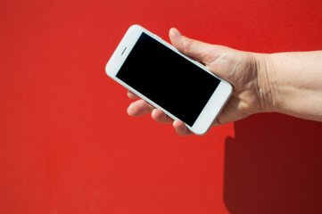 Close up on holding mobile smart phone over red background. Working remotely with information, modern communication lifestyle mock up display.