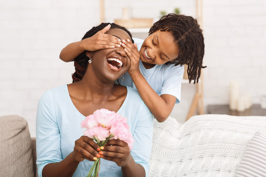 Afro girl congratulating her mom with flowers at home