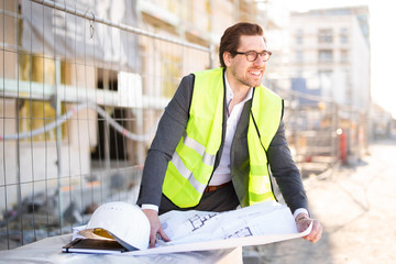 Freudig lächelnder Architekt auf der Baustelle mit Bauplänen 