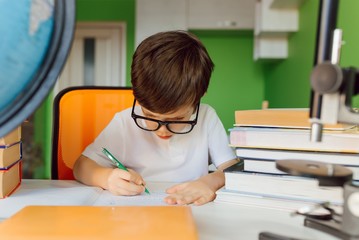 The boy is studying at home during CoVid-19 quarantine, distance learning online with a laptop, the child is doing homework for school. The schoolboy stayed at home.