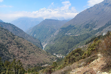 Fototapeta na wymiar Beautiful mountain valley with flowing river in Himalayas in the day. Kongde Ri mountain in the background. Mountainside is covered by forest. Beautiful landscape. Theme of travel in Nepal.
