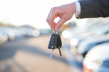 Autokauf, Verkäufer hält Zulassung Papiere und Schlüssel vor einer Reihe an Neuwagen