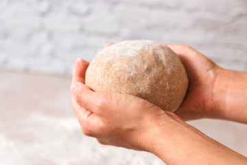 closeup woman hands holding kneaded dough from rye flour over marble countertop in bright kitchen. process of baking health bread at home