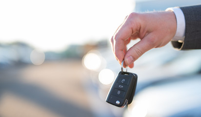 Autokauf, Verkäufer hält Zulassung Papiere und Schlüssel vor einer Reihe an Neuwagen