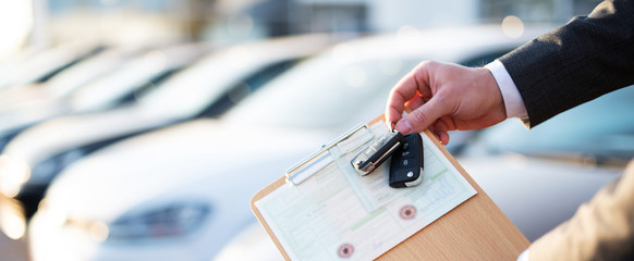 Autokauf, Verkäufer hält Zulassung Papiere und Schlüssel vor einer Reihe an Neuwagen - 336409795