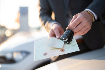 Autokauf, Verkäufer hält Zulassung Papiere und Schlüssel vor einer Reihe an Neuwagen