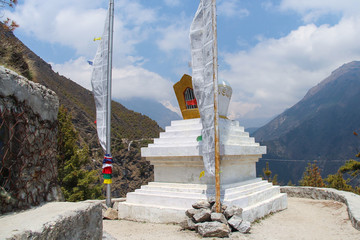 View of typical white stone tibetan buddhist stupa in Himalayas next to waving prayer flags. Clouds...