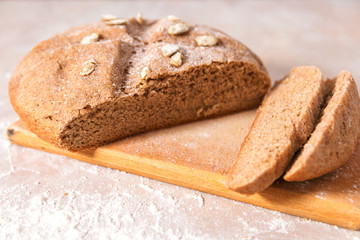 fresh home baked healthy bread from rye flour with pumpkin seeds on wooden rustic cutting board on marble countertop in bright kitchen