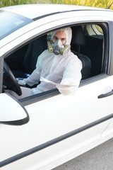 Dressed in full protective gear driver collects a sample from a man sitting inside his car as part of the operations of a coronavirus test
