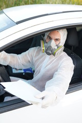 Dressed in full protective gear driver collects a sample from a man sitting inside his car as part of the operations of a coronavirus test
