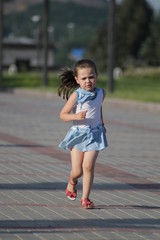 Fototapeta premium girl in blue and white clothes runs on the paving stones