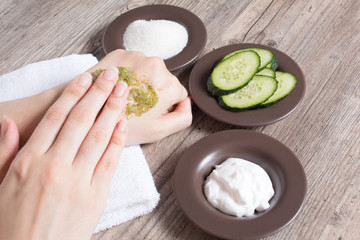 Skin care at home. A woman applies a natural homemade scrub to her hand. Ingredients for making the scrub, salt, sugar, cucumber, cream. Moisturizing, peeling, exfoliation, SPA, beauty salon. Eco