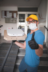 Fototapeta na wymiar Deliveryman with protective medical mask holding pizza box - days of viruses and pandemic, food delivery to your home.