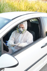 Dressed in full protective gear driver collects a sample from a man sitting inside his car as part of the operations of a coronavirus test
