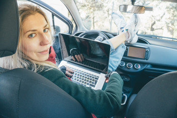 Young beautiful blonde hair woman working on laptop sitting inside a car