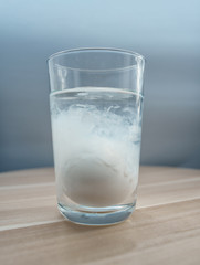 Glass cup with mineral water and an egg inside. The egg is dipped inside the glass and is enveloped in a white consistency. Close-up