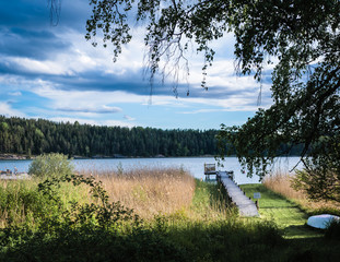 coastal view of the sea in Sweden, the footbridge enters the water and there are lounge chairs;...