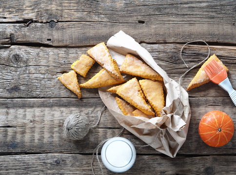 Glazed homemade scones sandwich pumpkin cookies, with tassel for glaze, in paper home packaging, on a wooden ancient background.View from above.