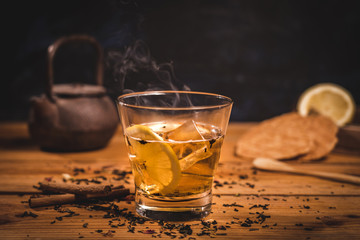 té con hielo y limon en vaso, con sus galletas, tetera y canela sobre mesa de madera