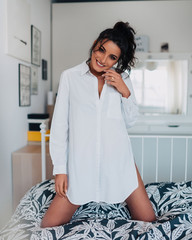 Beautiful sexy woman wearing a white shirt smiling on her bed at home