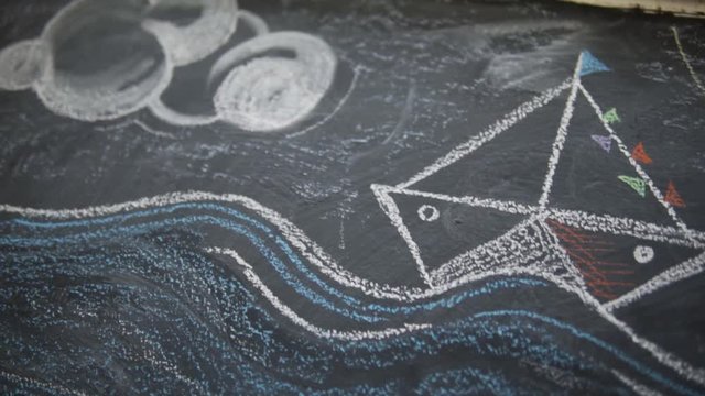 painting  with chalk on a black board  ,table ,plank showing a festive boat with colourful flags a blue sea with waves and yellow sun, artistic lifestyle, painting, draw , childhood memories, festive