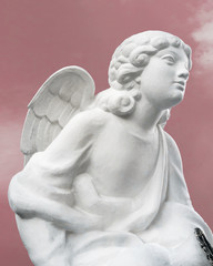 White statue of an angel isolated against the pink sunset sky. Angel looking forward