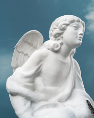 White statue of an angel isolated against a blue sky. Angel looking forward
