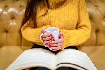 The woman who holds coffee in her hands and reads a book
