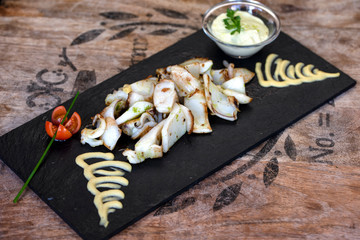 Traditional sea food. Typical Spanish food. Fried squid ration with mustard in a black stone plate.