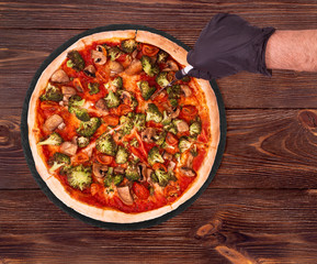 Pizza with veggie vegetables, on slate bottom, on wooden table hand cutting pizza, top view