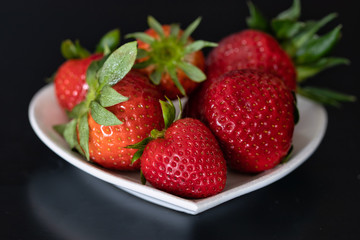 fresh strawberry piece on dark table. Raw juicy strawberry heart shape white plate. black background.