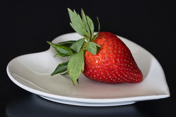 fresh strawberry piece on dark table. Raw juicy strawberry heart shape white plate. black background.