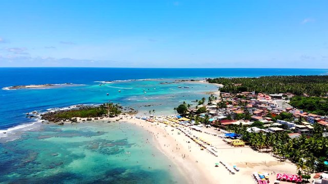 Cinematic aerial of Morro de Sao Paulo blue turquoise beaches, tourists enjoying the beach and sun, and green nature. Bahia, Brazil. Drone slowly moving left