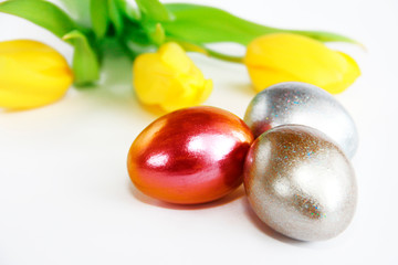 shiny multicolored easter eggs and yellow tulips with green leaves