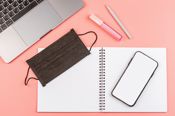 Top View Of Workspace Desk With Laptop, Blank Notebook, Medical Mask on pink background. Flat lay, nobody, copy space, mockup, template. Working from home, stay at home during Pandemic covid-19.